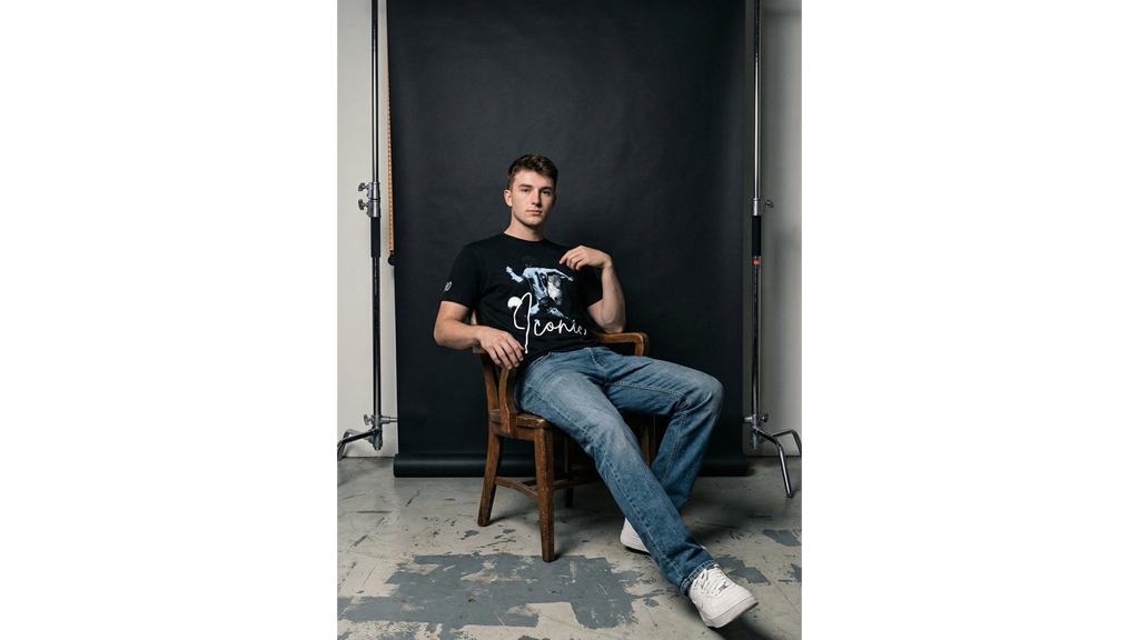 Man sitting on a chair in front of a black backdrop in a studio setting.