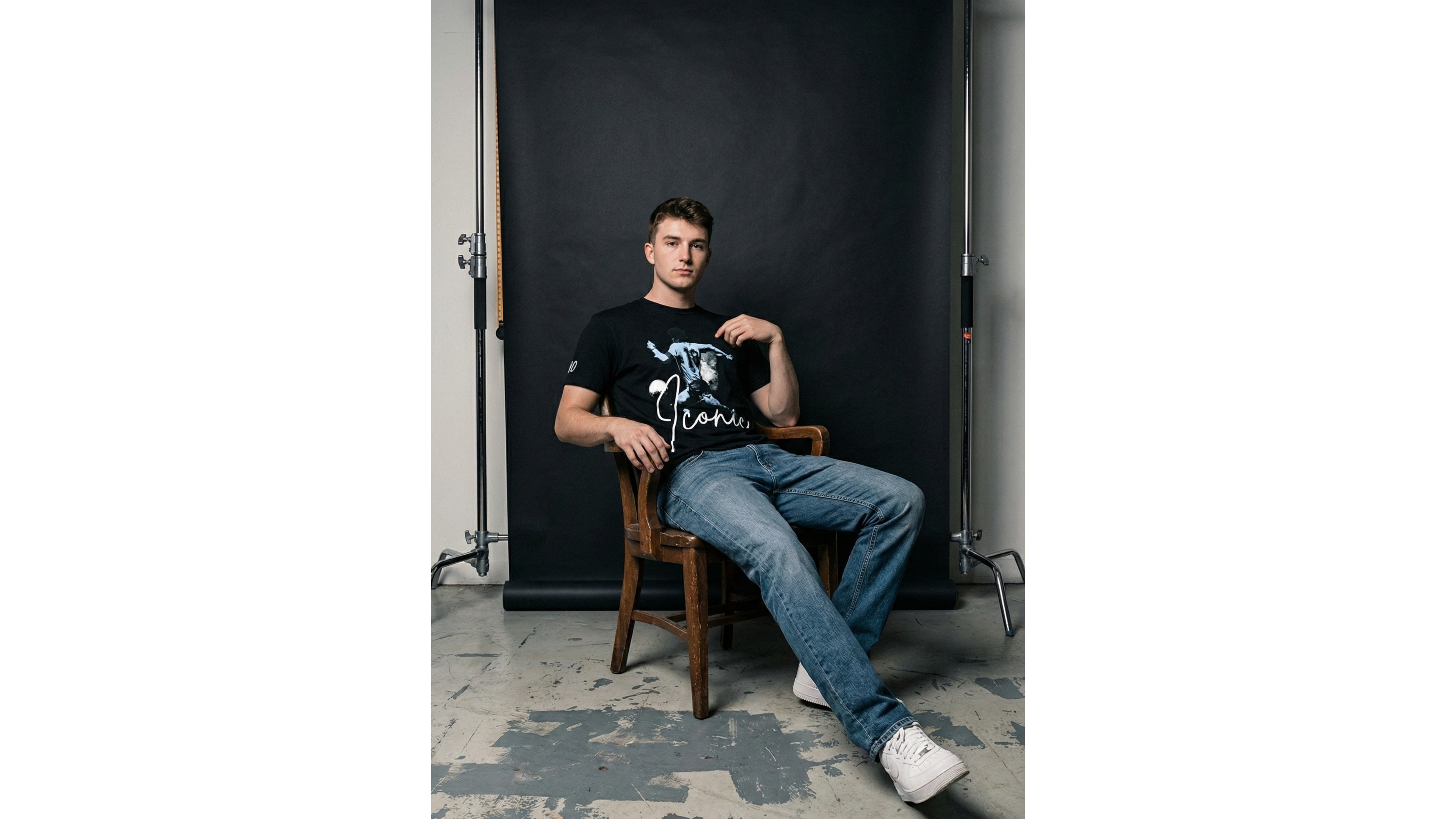 Man sitting on a chair in front of a black backdrop in a studio setting.